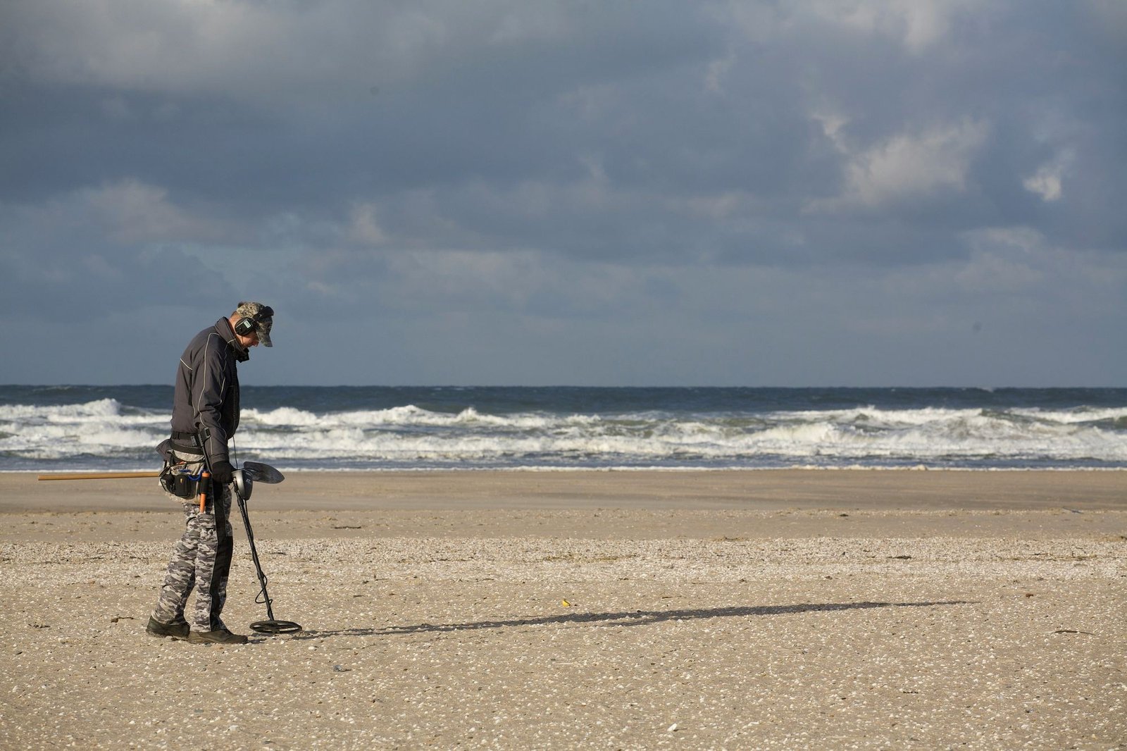 A detectorist working the wet sand at the surf line